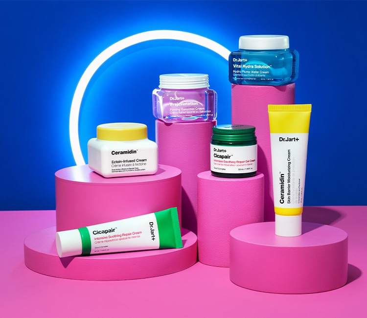 A group of Dr.Jart+ skincare products displayed on pink cylindrical platforms against a blue background with a neon circle.